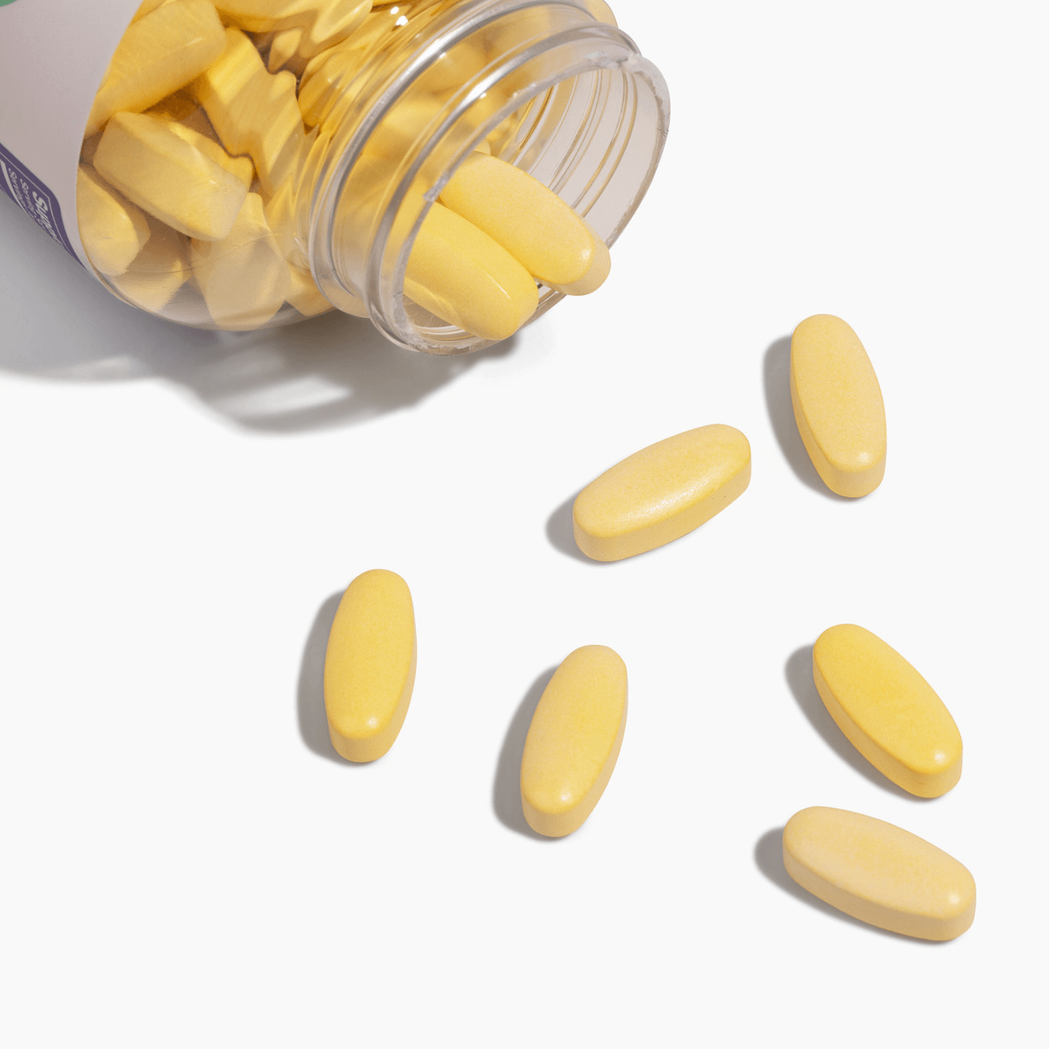 Complete Bariatric Vitamin Formula Tablets spilling from a bottle, yellow tablets on a white background.